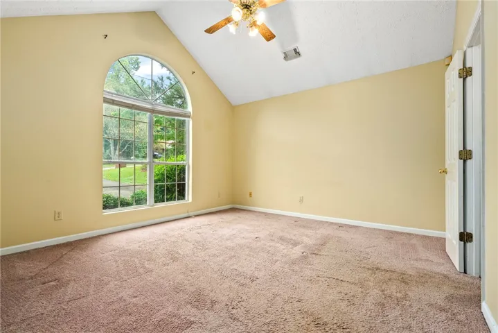 A spacious room features a vaulted ceiling, grand arched window, and warm carpet.