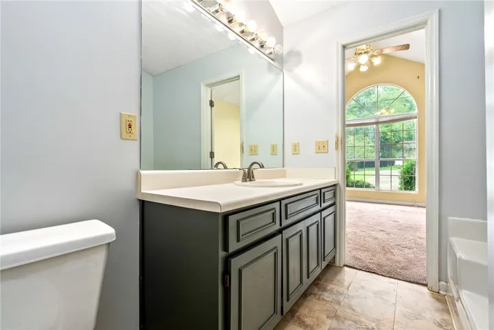Vanity with an integrated sink and mirror, offering a clear view into a sun-drenched room through an arched window.