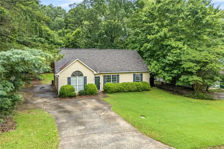 A welcoming abode nestled amongst mature trees, featuring a concrete driveway and verdant lawn.