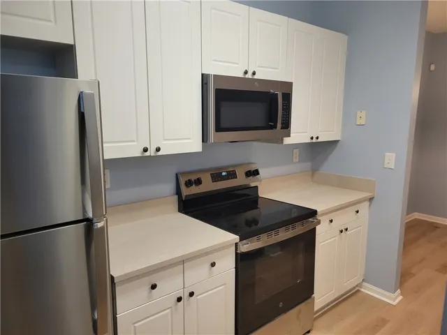 A compact kitchen with white cabinetry and stainless steel appliances awaits culinary endeavors.
