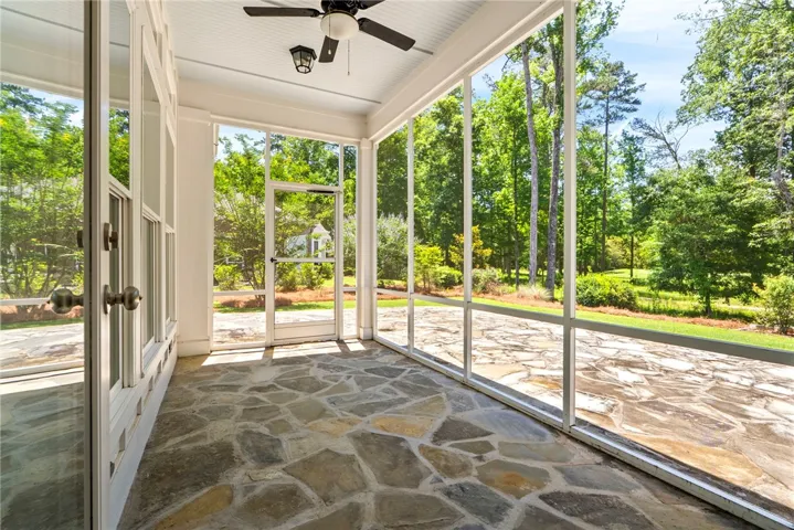 A spacious screened porch with natural stone flooring offers serene views of mature trees and landscaping.
