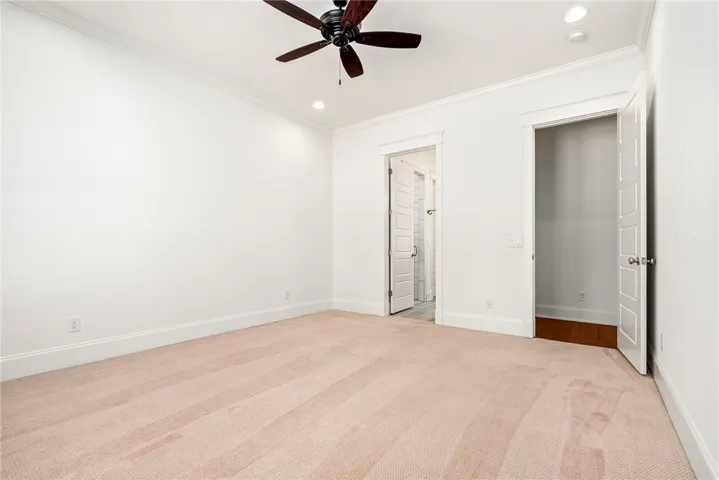 An inviting room with pristine white walls, light carpet, and a ceiling fan offers a comfortable living space.