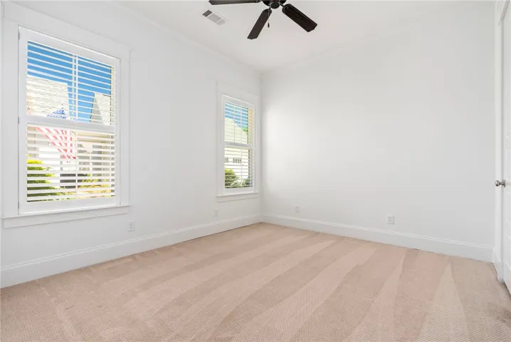 A well-lit bedroom features plush carpet flooring and a ceiling fan for comfort.
