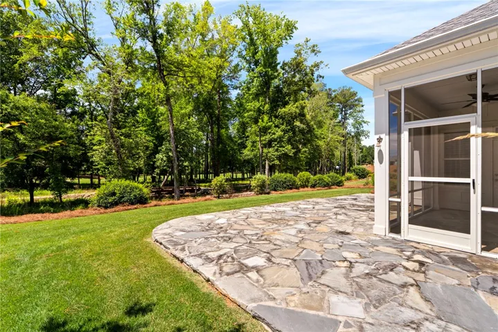 A spacious, flagstone patio adjoins a lush green yard and screened-in porch, ideal for outdoor gatherings.