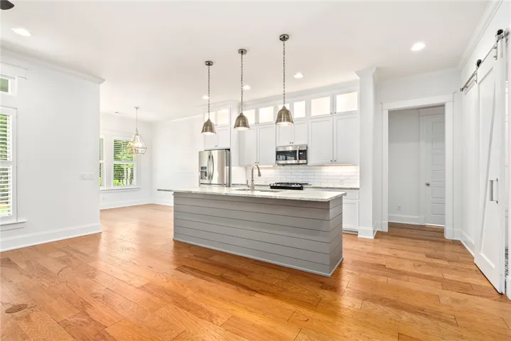 A well-lit kitchen with sleek stainless steel appliances, a generous island, and rich hardwood flooring.
