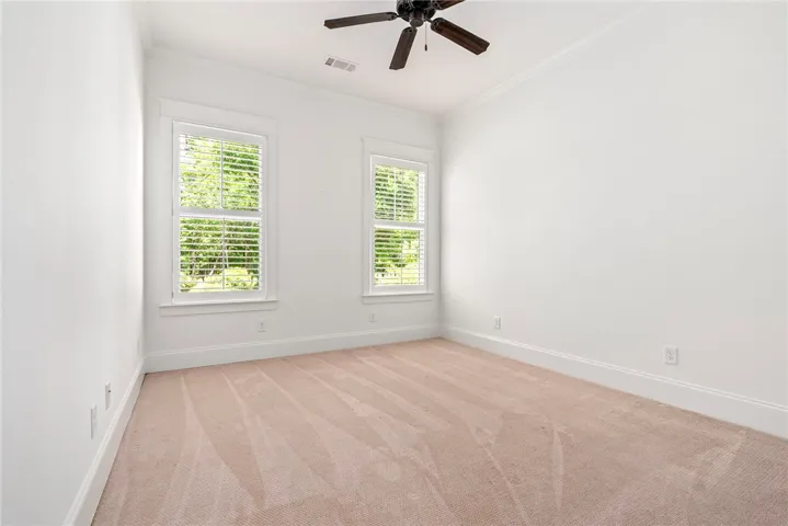 A quiet, naturally illuminated bedroom, featuring plush carpeting and a modern ceiling fan for optimal comfort.