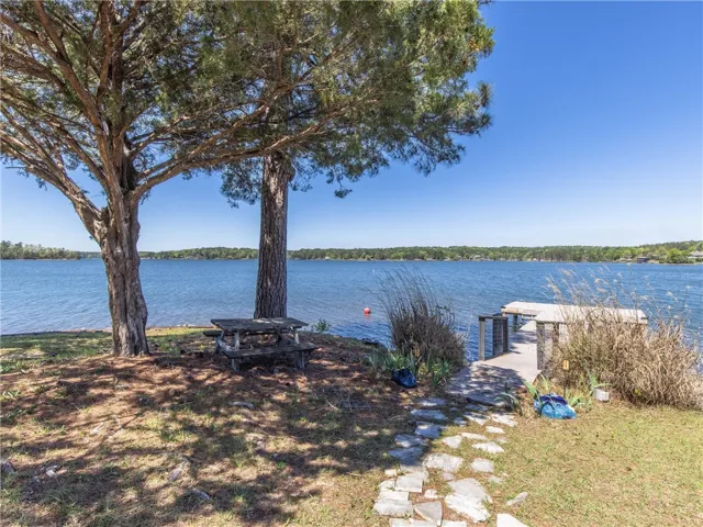 A tranquil lakeside retreat with mature trees providing ample shade, a picnic area, and private dock access.