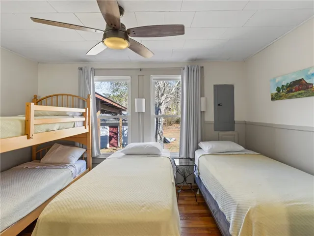 A well-lit bedroom features hardwood floors and a ceiling fan, with ample natural light from multiple windows.