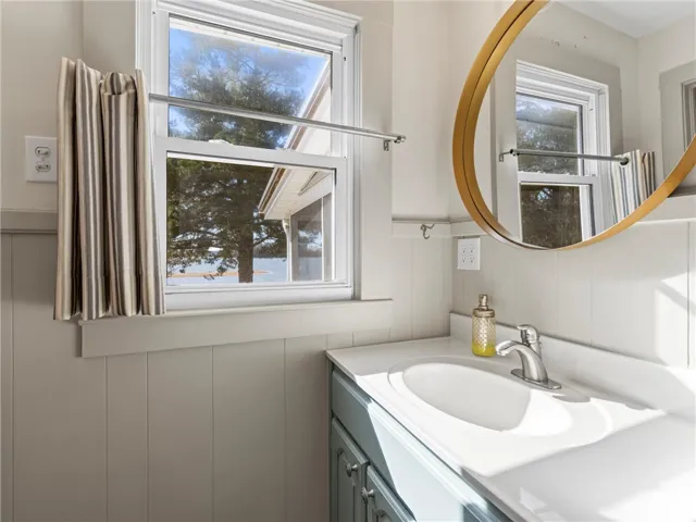 A well-appointed bath with a vanity, sink, and round mirror offers tranquil views through a window.