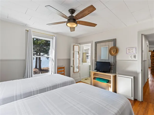 A tranquil bedroom with hardwood floors offers cooling ceiling fan and water views from a large window.