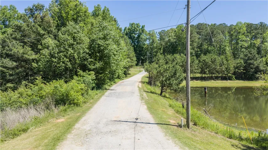 A private gravel road winds through lush trees, leading to a tranquil pond, perfect for serene living.