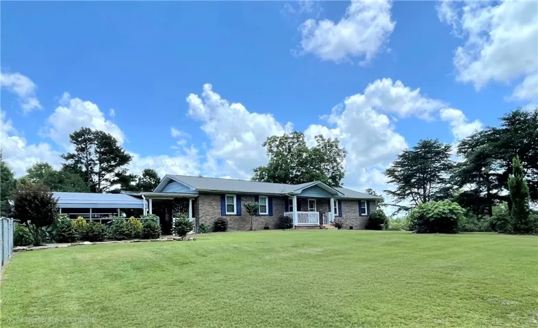 A classic brick home set on a beautiful lawn, surrounded by mature trees under a brilliant sky.