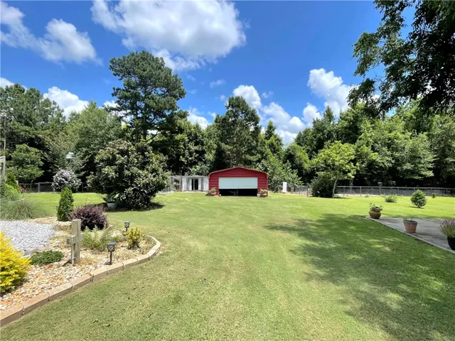 A sprawling green lawn extends towards a useful shed, framed by mature trees under a vast sky.
