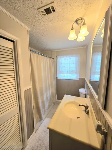 A compact bathroom featuring a functional vanity and a full shower with tiled walls.