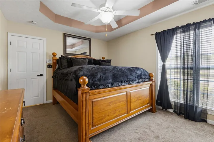 A comforting bedroom features a ceiling fan, soft carpeting, and a sun-filled window with blinds.