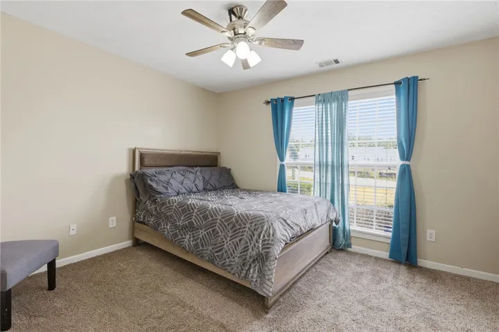 A comfortable bedroom features plush carpeting and a large window, offering ample natural light.