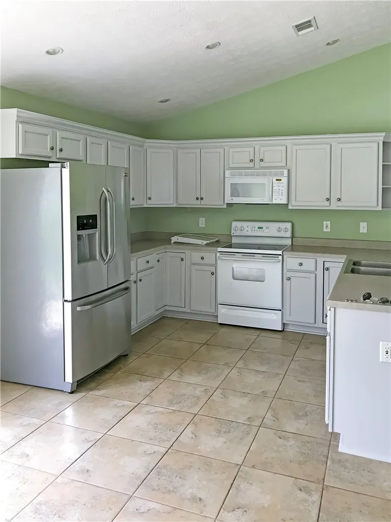 Vast tile flooring grounds this functional kitchen, featuring ample white cabinetry and modern appliances.