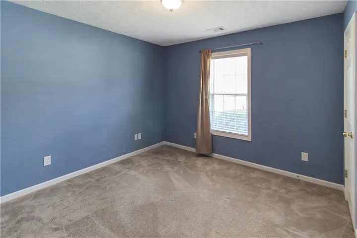 A well-lit bedroom features plush carpeting and a bright window with neutral drapes.