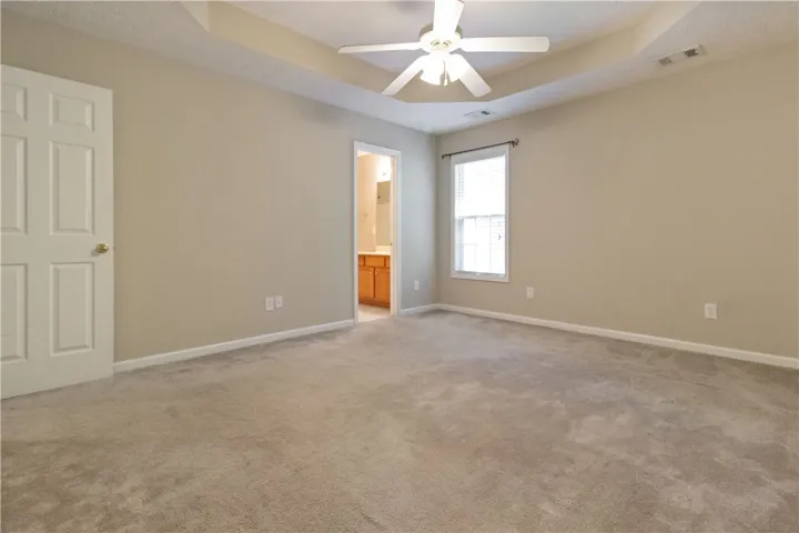 A spacious primary bedroom with a tray ceiling and plush carpeting for comfortable living.