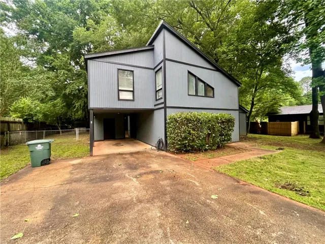 A modern facade with striking geometric windows and a concrete driveway, nestled amidst lush trees.