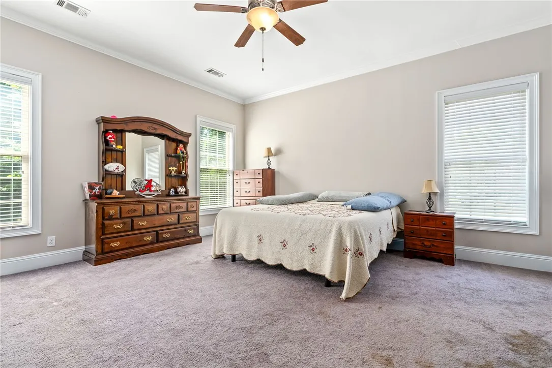 Relaxation awaits in this generous bedroom, featuring multiple windows and soft carpeting.