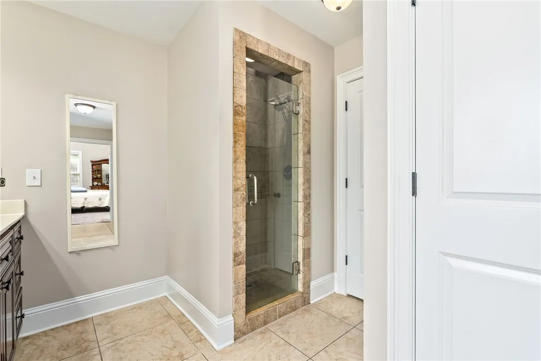 A pristine tiled floor anchors this primary bathroom, featuring a sleek, frameless glass shower.