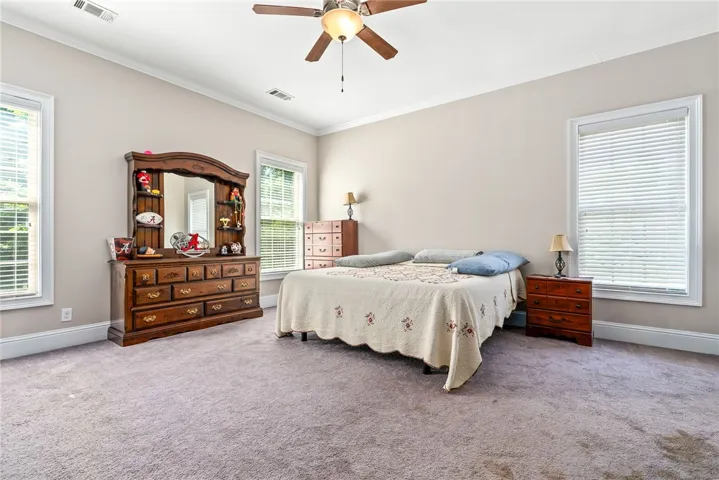 Relaxation awaits in this generous bedroom, featuring multiple windows and soft carpeting.