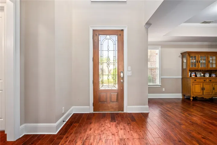 A rich wooden door with artistic glass accents invites you into a home featuring gleaming hardwood floors.