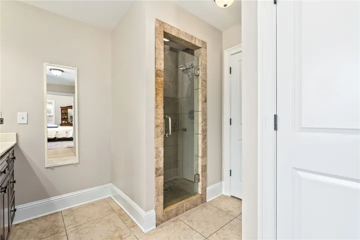 A pristine tiled floor anchors this primary bathroom, featuring a sleek, frameless glass shower.