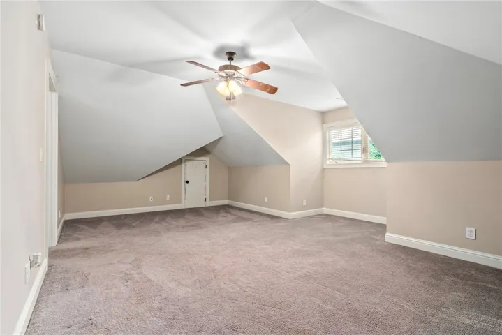 A spacious attic retreat features a modern ceiling fan, ample carpeting, and a window for natural light.