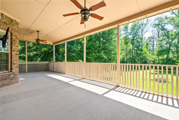 An inviting covered patio with ceiling fans overlooks a serene, wooded landscape.