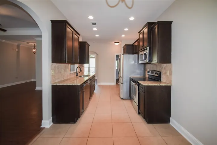 A galley kitchen with dark cabinetry, stone countertops, and integrated stainless steel appliances awaits culinary endeavors.