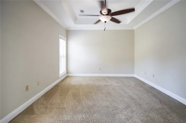A quiet bedroom featuring plush carpet and a stylish tray ceiling with a modern ceiling fan.