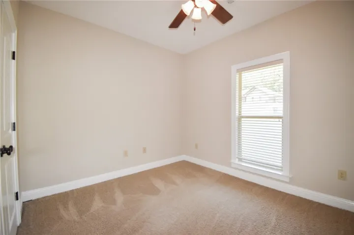 A well-lit bedroom features plush carpeting and a bright window with neutral walls.
