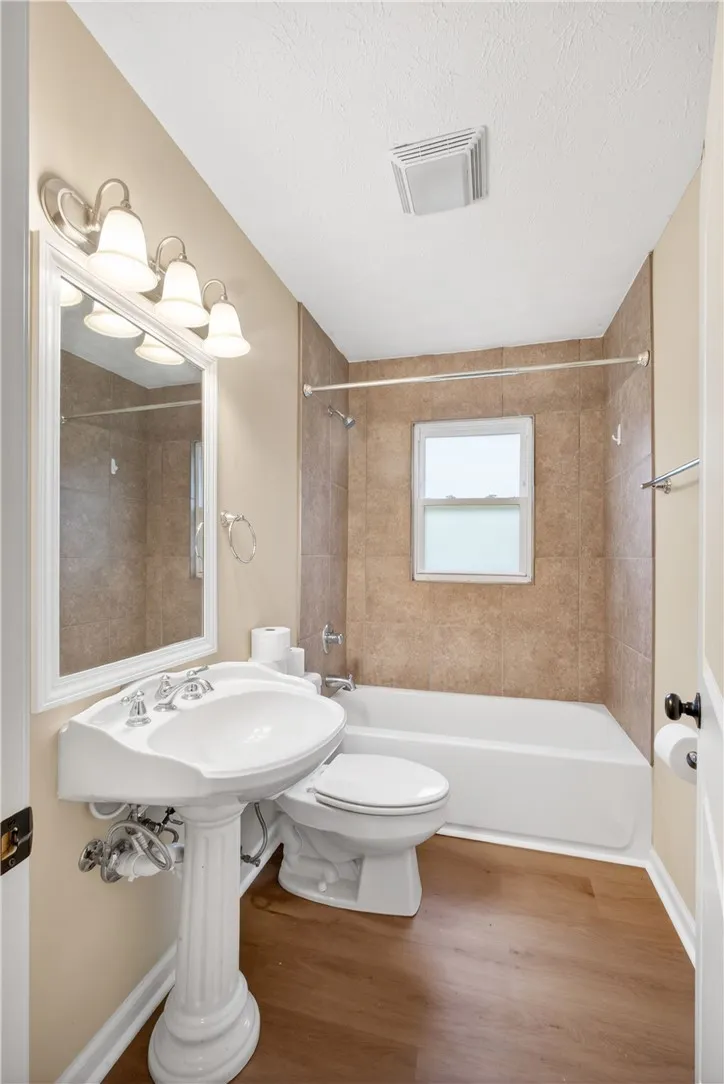 A well-appointed bath with pedestal sink, full shower, and natural wood-look flooring provides both style and utility.