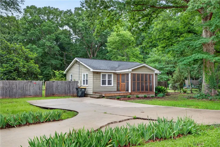 A charming cottage-style residence nestled among mature trees, featuring a welcoming screened porch.