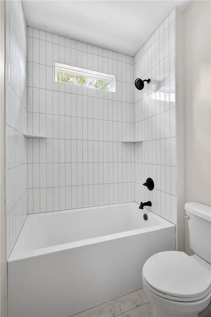 A sleek, fully tiled bath and shower combo offers a private window and modern fixtures.