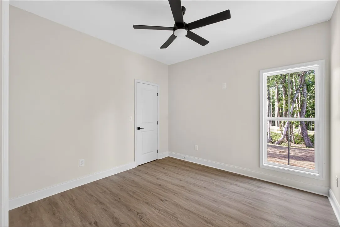 A quiet bedroom featuring resilient wood flooring and verdant tree views from the window.