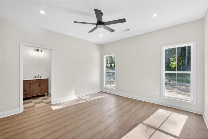 Well-lit primary bedroom featuring durable wood flooring and direct access to a private bathroom.