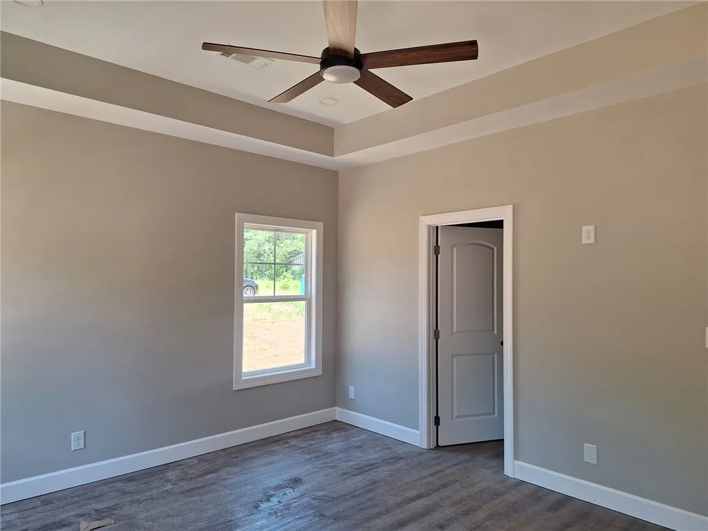 A quiet bedroom retreat features a tray ceiling with a modern ceiling fan and durable flooring.