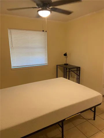 A comfortable bedroom with efficient ceiling fan cooling and durable tile flooring.