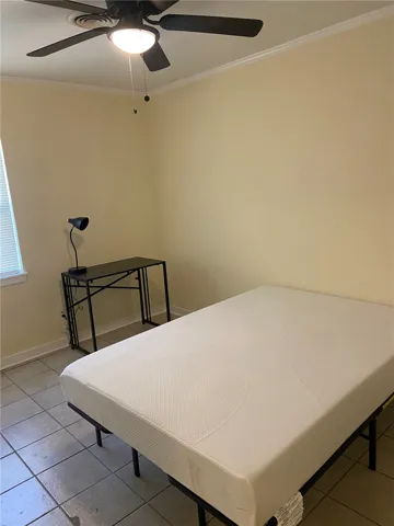 A comfortable bedroom with tile flooring, featuring a ceiling fan for optimal airflow.