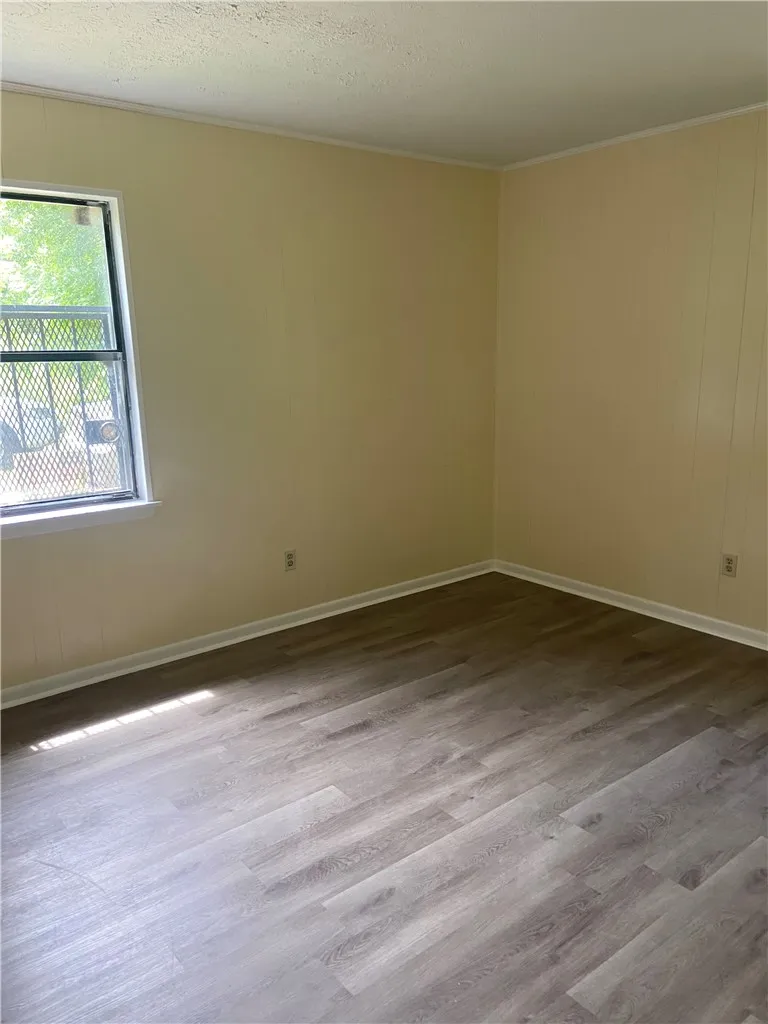 Well-lit room with durable wood-look flooring and a secure window for natural light.