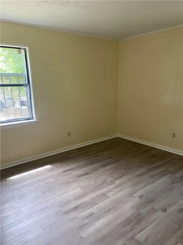Well-lit room with durable wood-look flooring and a secure window for natural light.