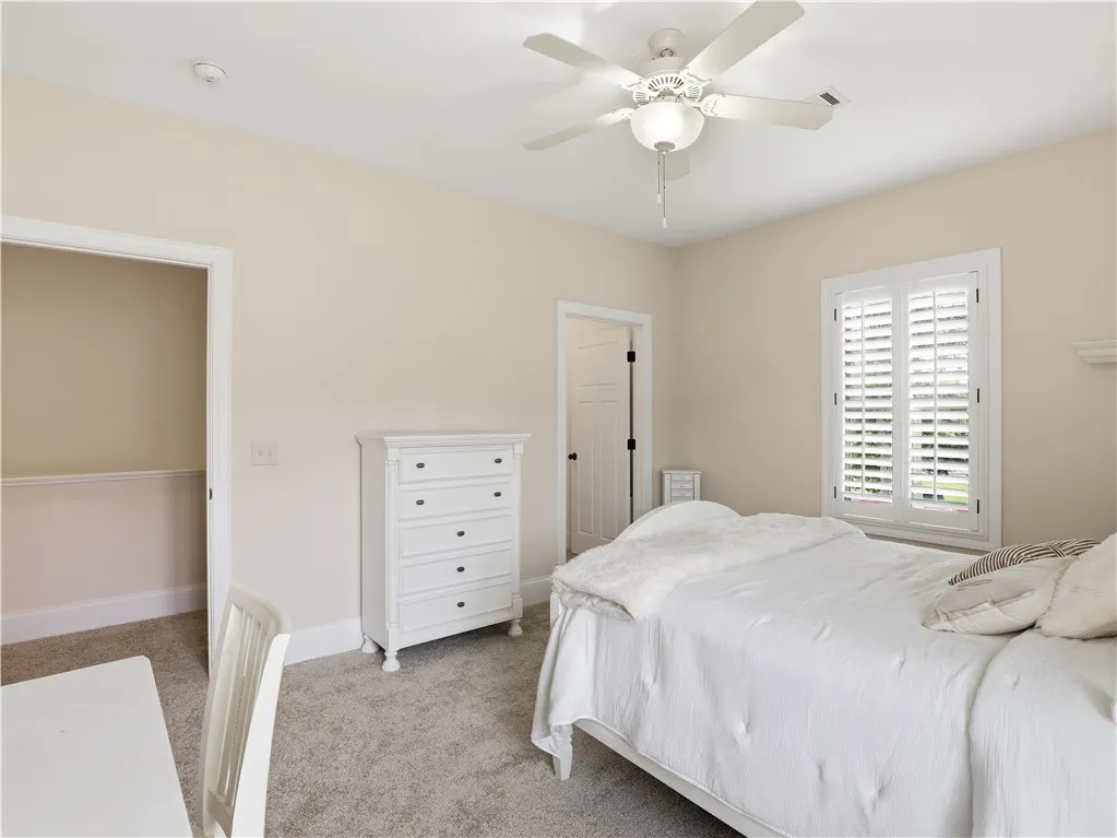 A well-lit bedroom features plush carpeting and a modern ceiling fan, ideal for comfort.