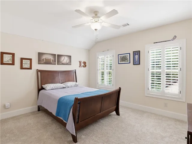 A comfortable bedroom features carpet flooring and a ceiling fan, with natural light filtering through window shutters.