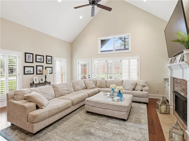 Vast living space with vaulted ceilings and rich hardwood flooring, anchored by a brick fireplace.