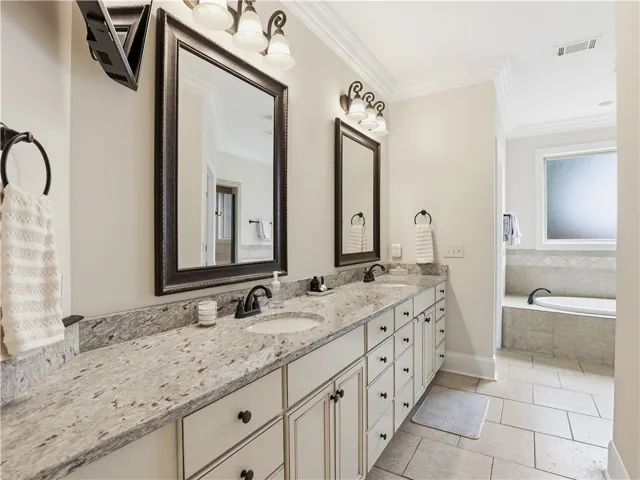 Elegant primary bath featuring a dual vanity with granite counters, tile flooring, and a separate soaking tub.