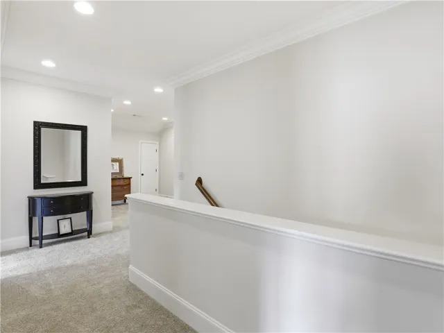 Elegant crown molding adorns this hallway, complemented by plush carpet and ample recessed lighting.