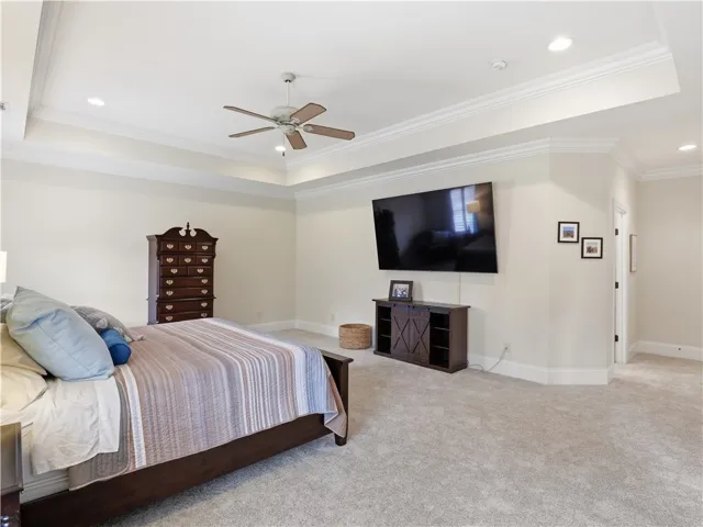 A spacious primary bedroom features tray ceilings, crown molding, and plush carpeting.